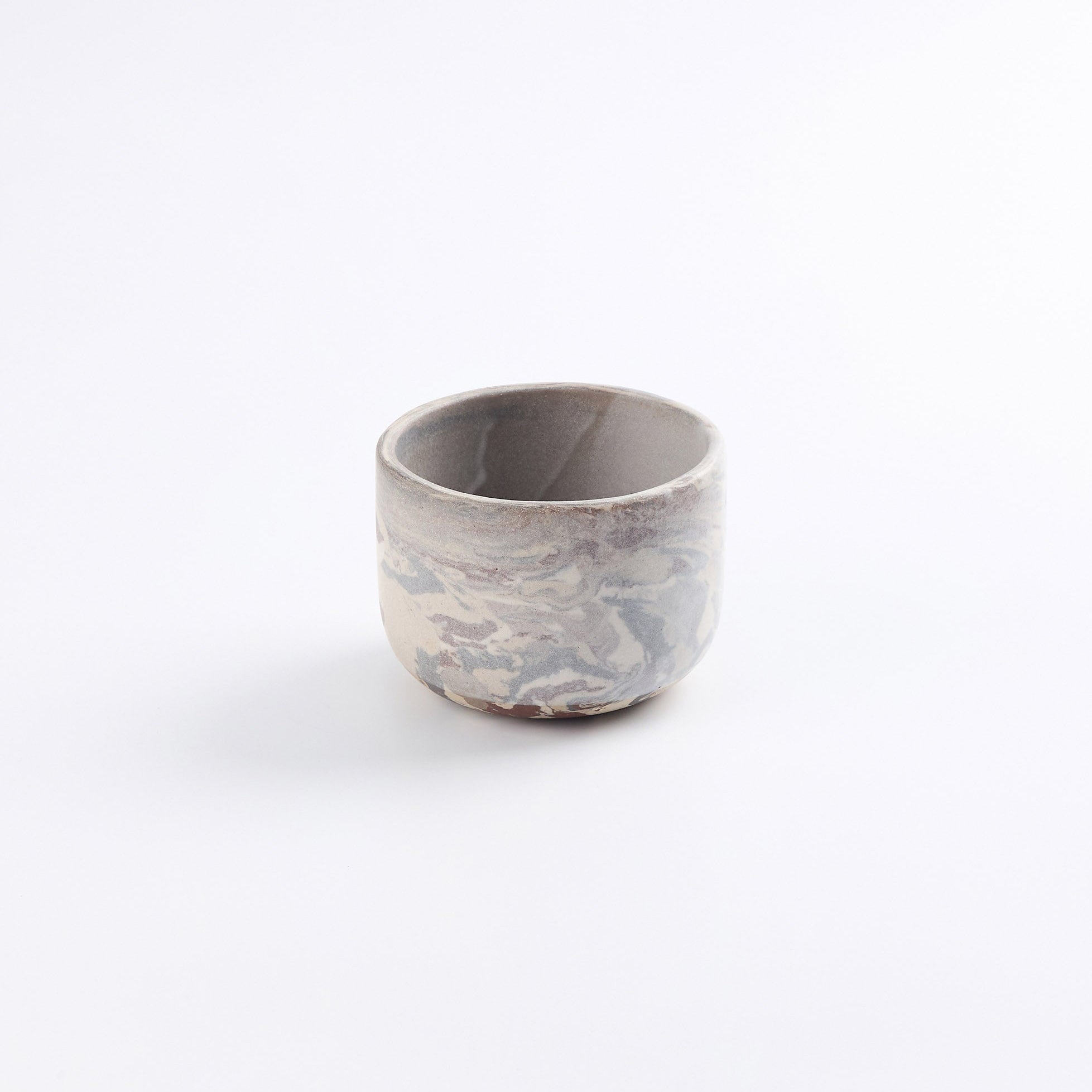 Handmade stoneware coffee cup without a handle, abstract marbled clay design using brown, black, red and natural clay with a pure matte white glaze on a white background.