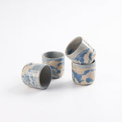 Four cups with marbled patterns of blue, white and beige clay and gloss surface. Stacked with a white background. 