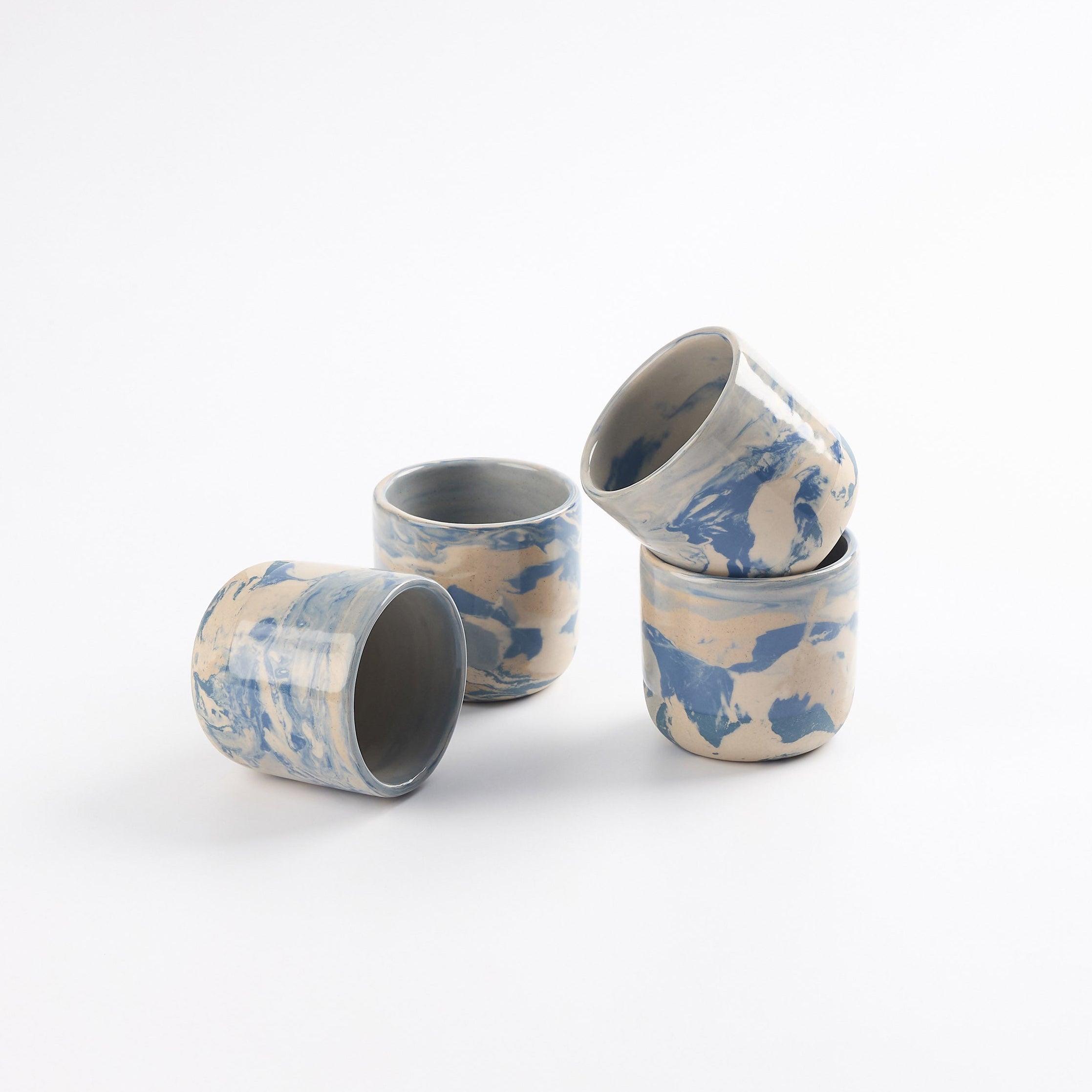 Four cups with marbled patterns of blue, white and beige clay and gloss surface. Stacked with a white background. 