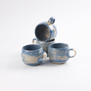 Stacked set of four cobalt blue ceramic mugs on a white background