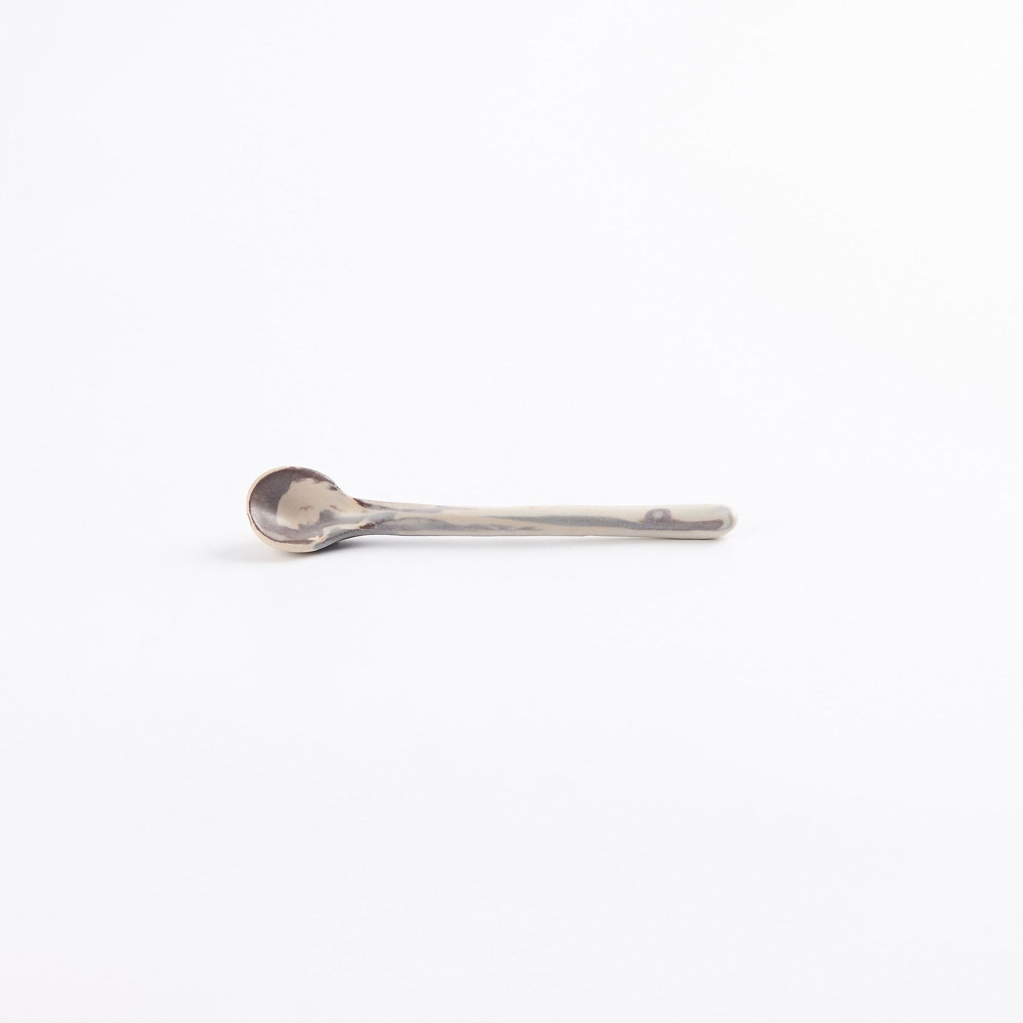 Handmade ceramic teaspoon in abstract marbled clay design with use matte white glaze on a white background.