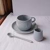 Handmade blue speckle coffee and tea mug by Palinopsia Ceramics with a teaspoon, and small ceramic milk pourer. 