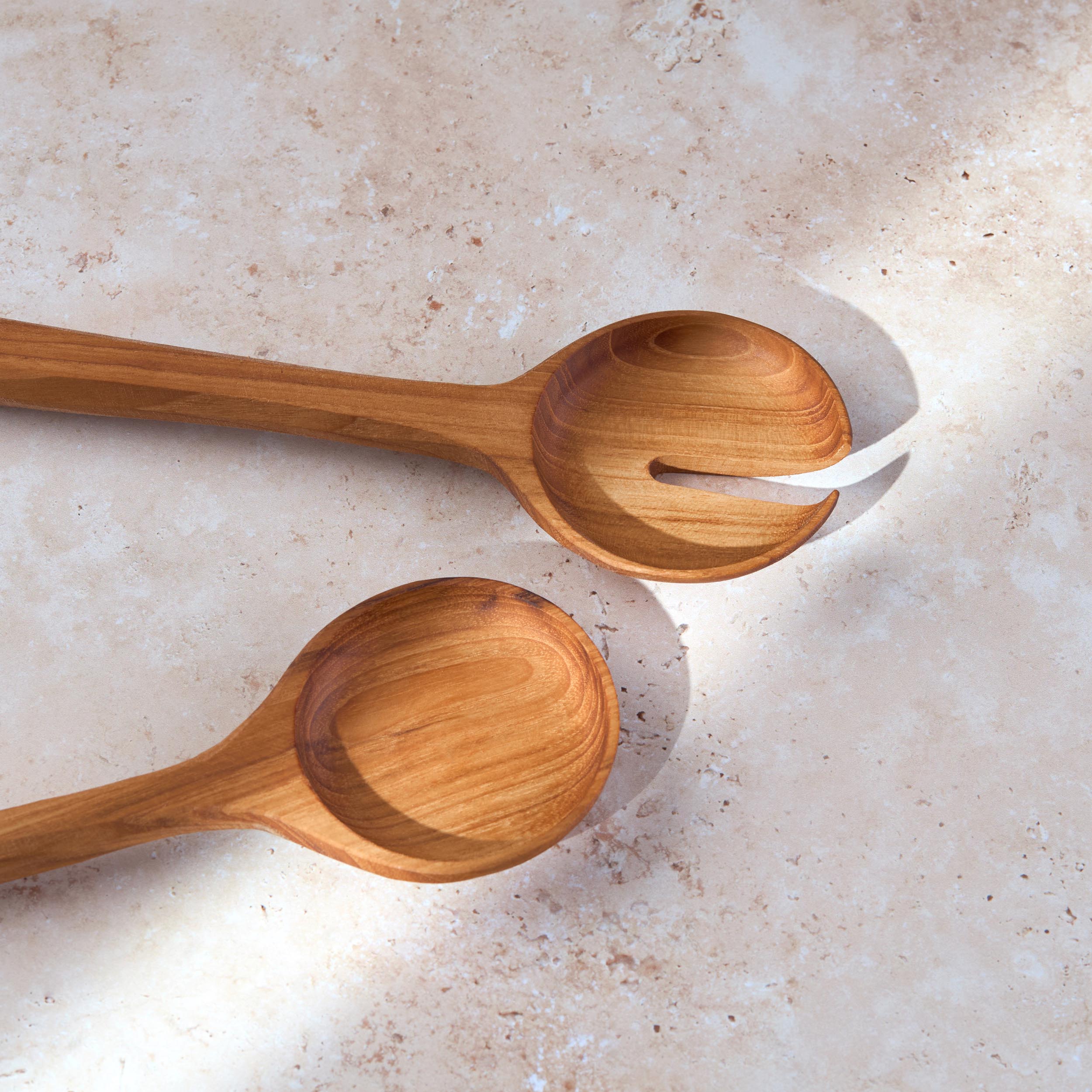 Detailed shot of a retro teak wooden salad serving set by Palinopsia on a light stone background.