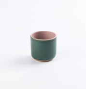 Green stoneware ceramic cup with pink interior on a white background