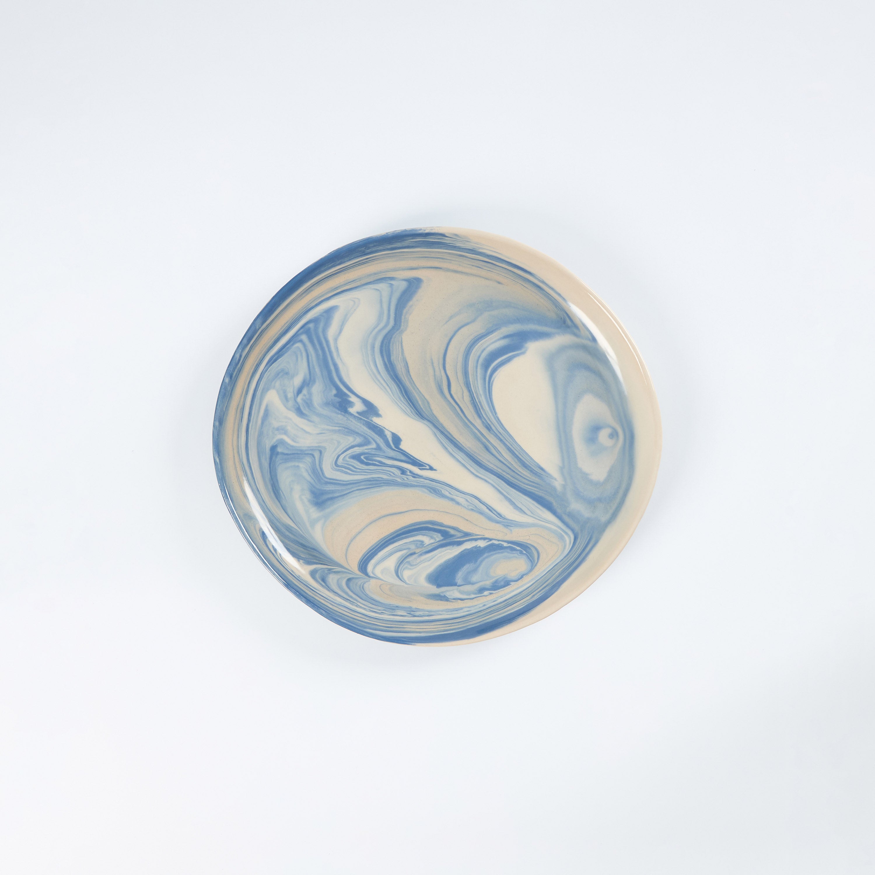 Handmade ceramic plate with a marbled clay pattern in cobalt blue, beige and cream on a white background by Palinopsia