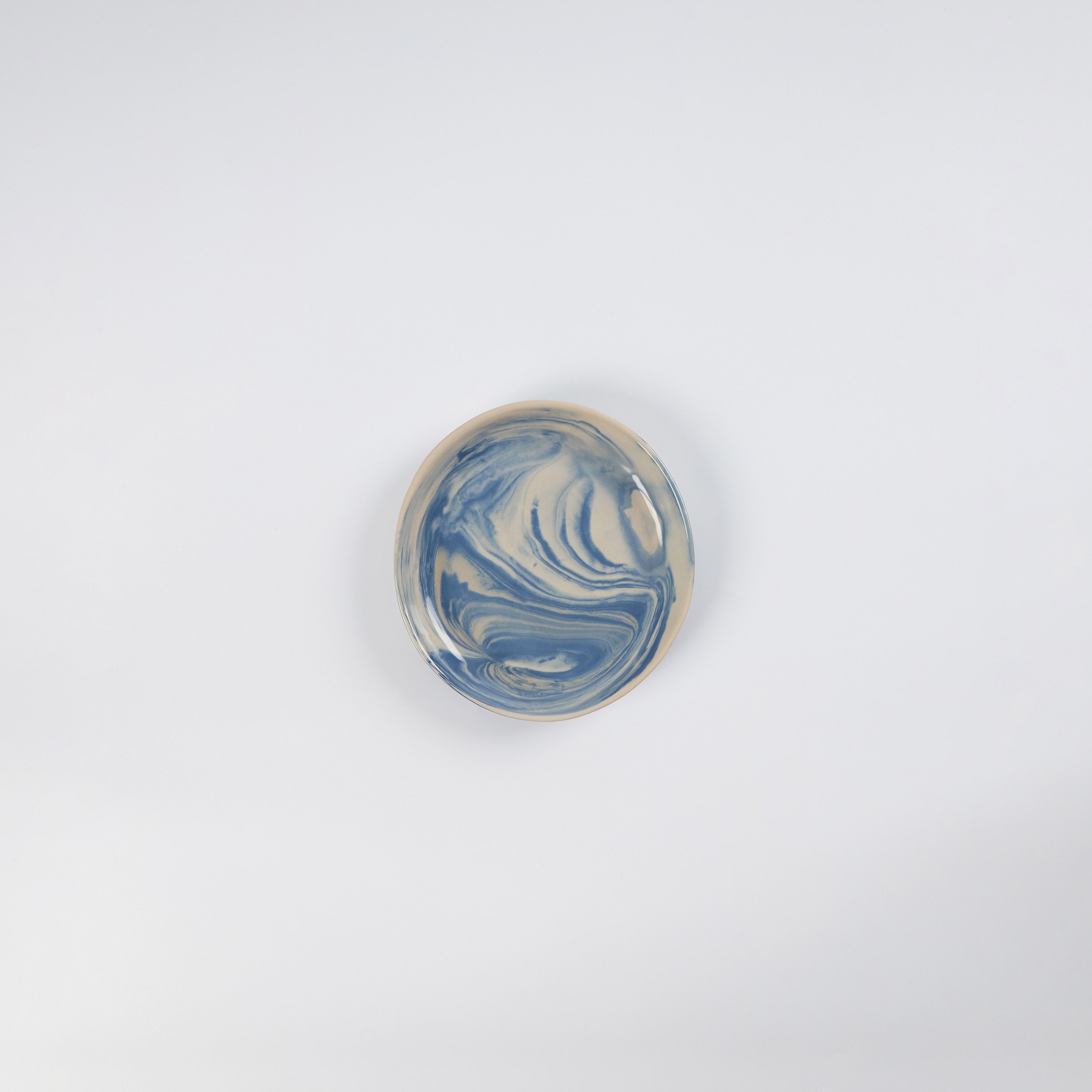Small handmade ceramic plate with a marbled clay pattern in cobalt blue, beige and cream on a white background by Palinopsia