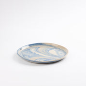 Handmade ceramic plate with a marbled clay pattern in cobalt blue, beige and cream on a white background by Palinopsia