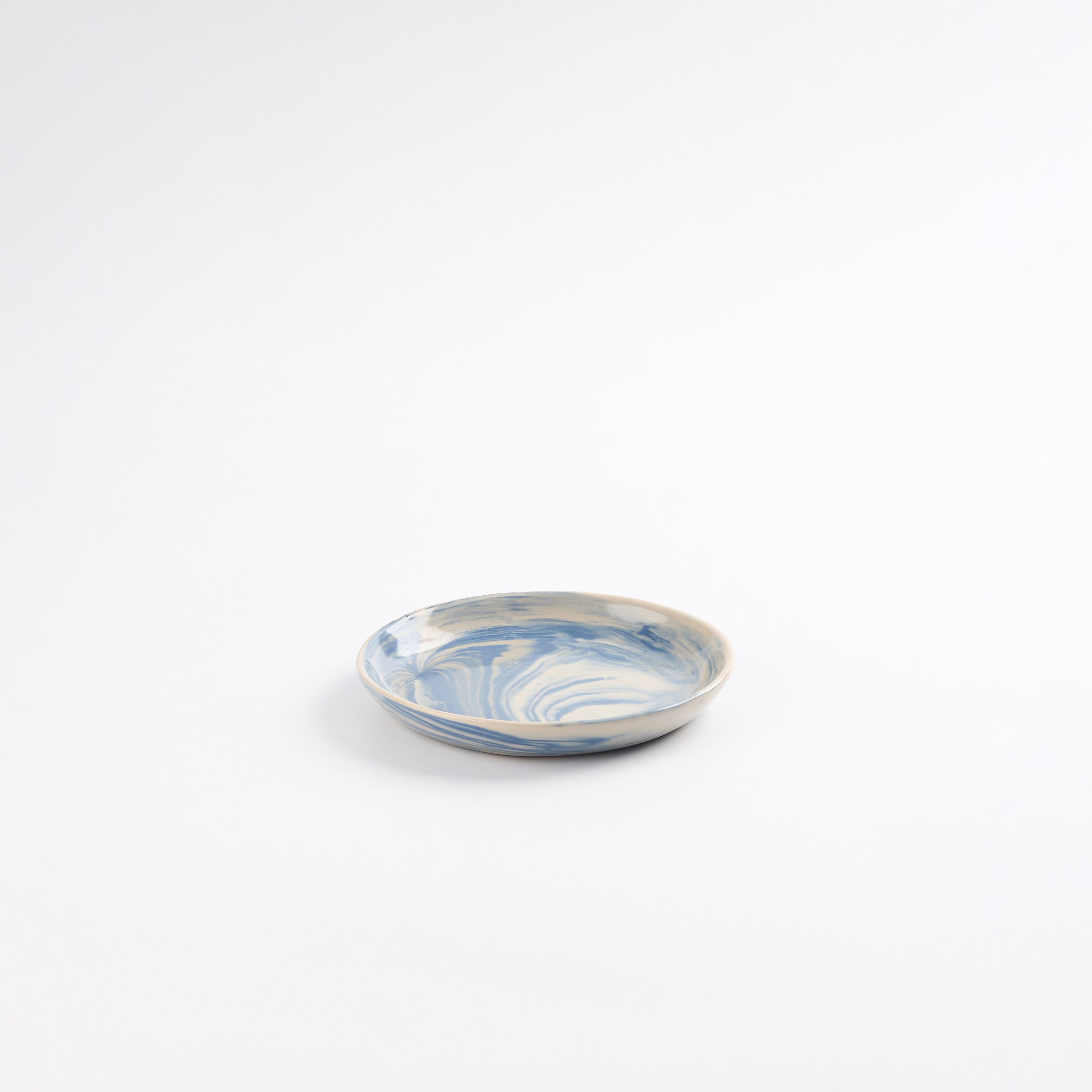 Small handmade ceramic plate with a marbled clay pattern in cobalt blue, beige and cream on a white background by Palinopsia
