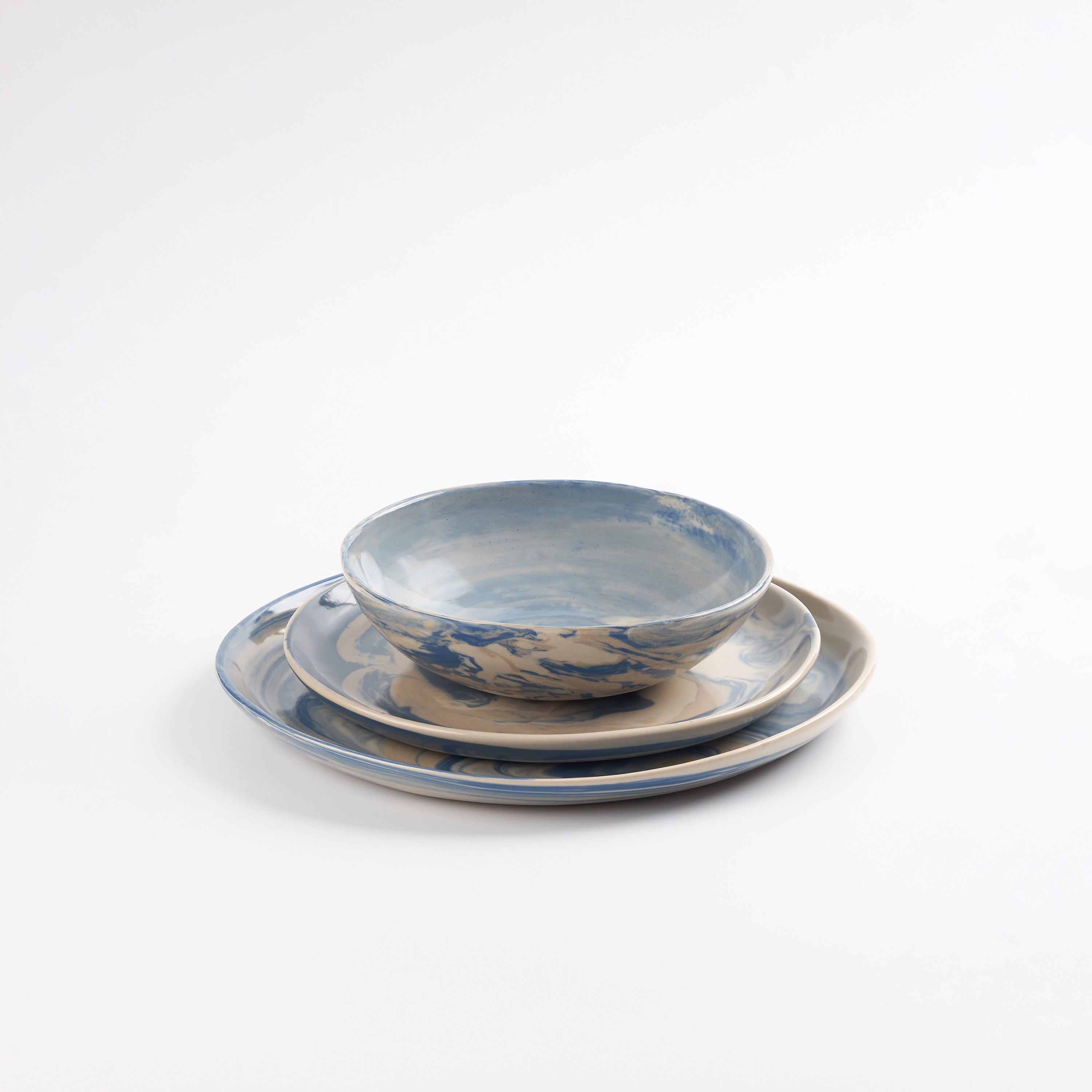 Three piece handmade ceramic dinner set with a marbled clay pattern in cobalt blue, beige and cream on a white background by Palinopsia