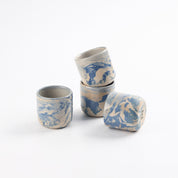 Four cups with marbled patterns of blue, white and beige clay and gloss surface. stacked with a white background. 