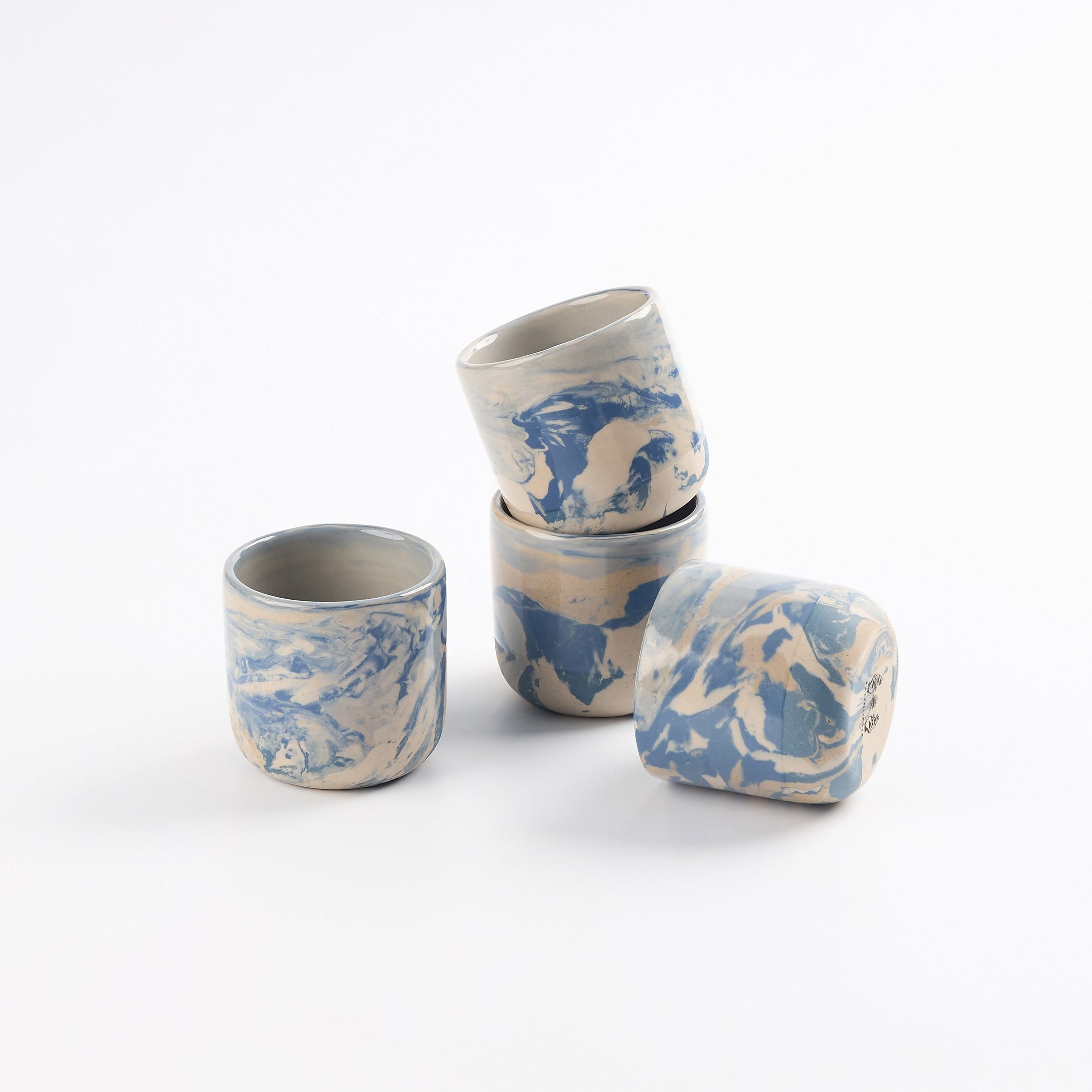 Four cups with marbled patterns of blue, white and beige clay and gloss surface. stacked with a white background. 