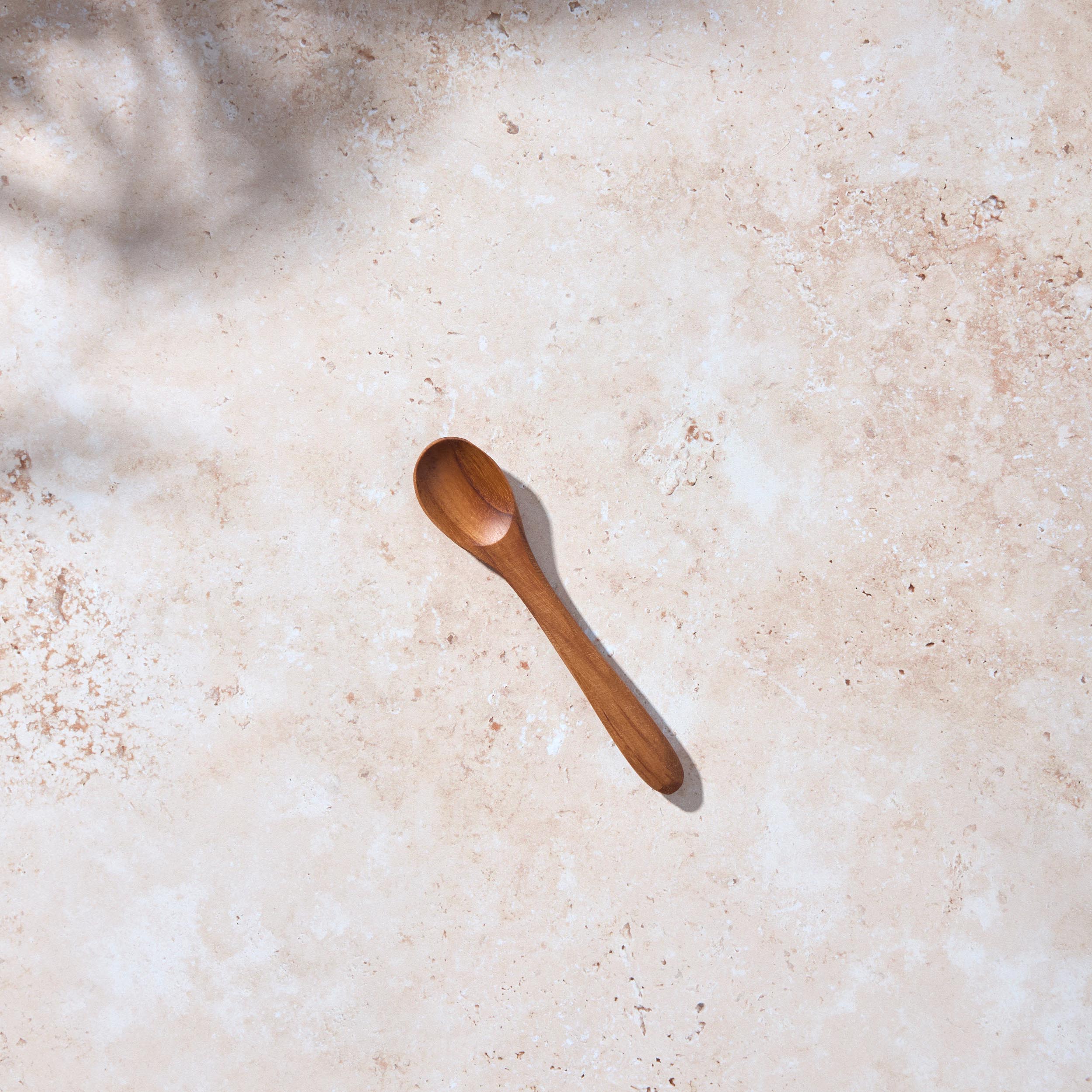 Bird’s-eye view of a Palinopsia small wooden teak spoon on a light stone background.