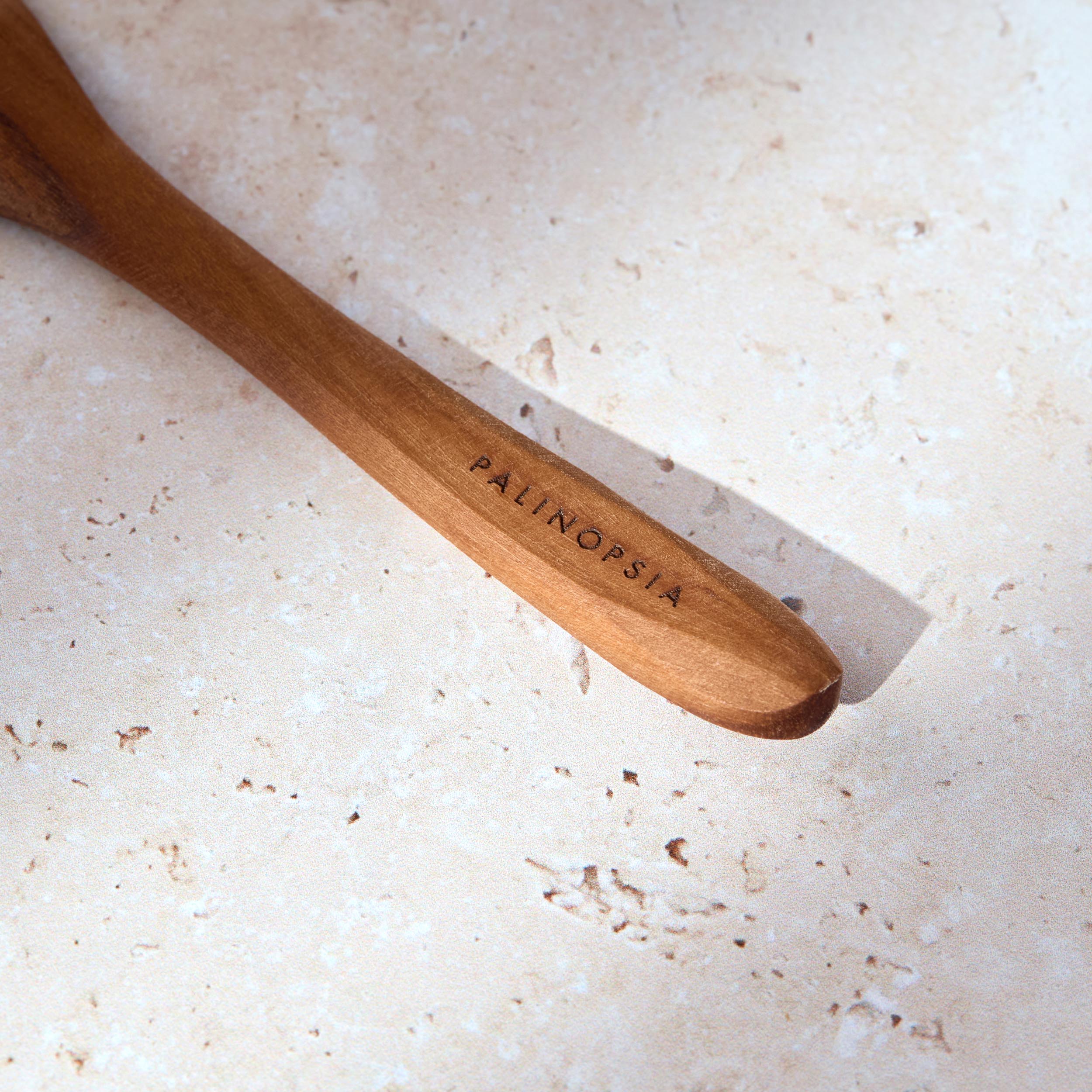 Close-up shot of the handle of a teak wooden olive spoon with a Palinopsia label on the handle.