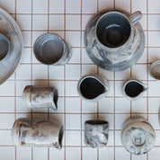 Palinopsia Marbled clay ceramic dinnerware mugs cups and hand pourers on tiled kitchen bench