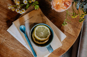 Teacup with lemon slice on a book, surrounded by flowers on a wooden surface