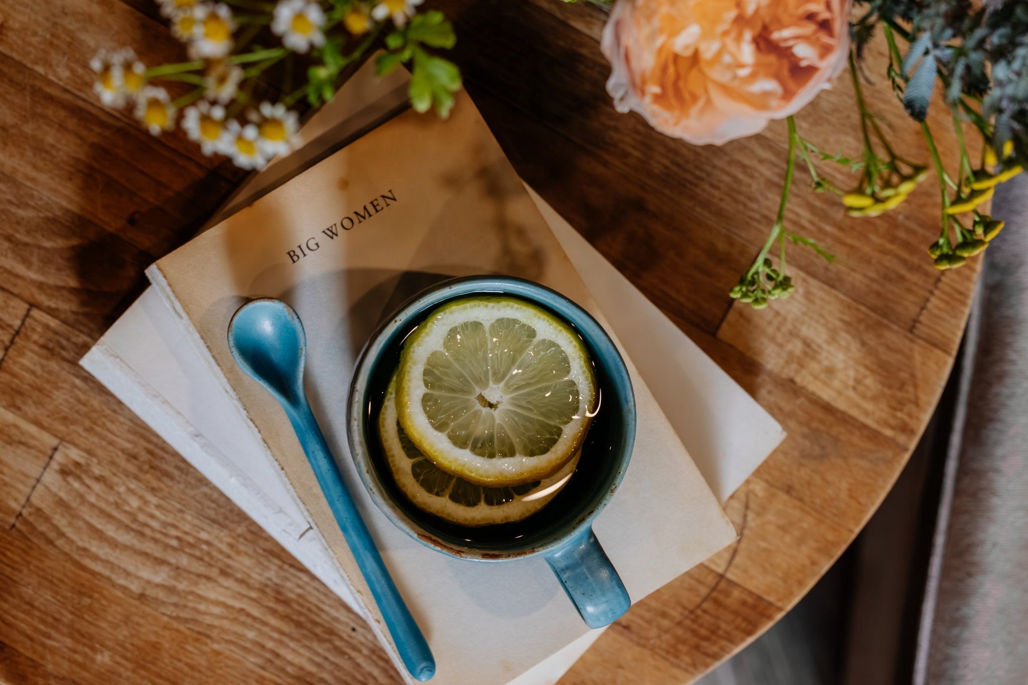 Teacup with lemon slice on a book, surrounded by flowers on a wooden surface