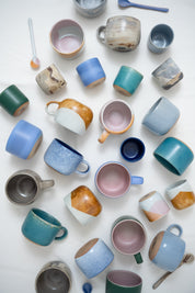 Colourful cups and mugs spread out on a white surface showing colour