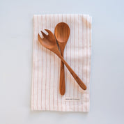 Palinopsia Teak wooden spoons on a striped linen tea towel with a light blue background