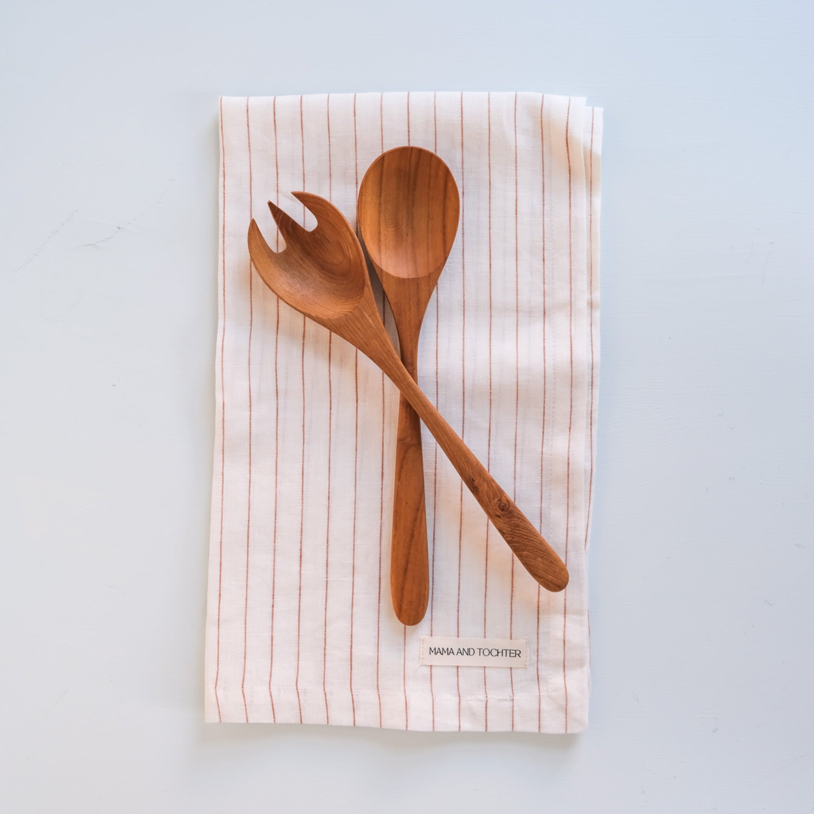 Palinopsia Teak wooden spoons on a striped linen tea towel with a light blue background