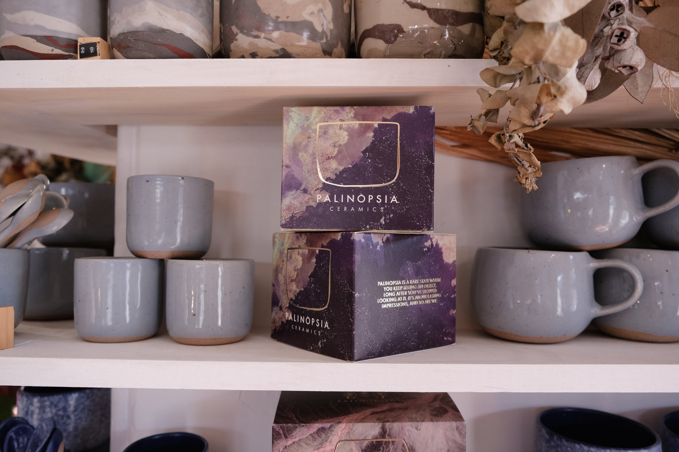 Shelves with blue grey mugs and cups with Palinopsia boxes in a store setting