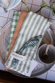 Set of green and white striped tea towels on a tiled surface with a Palinopsia teacup and spoon.