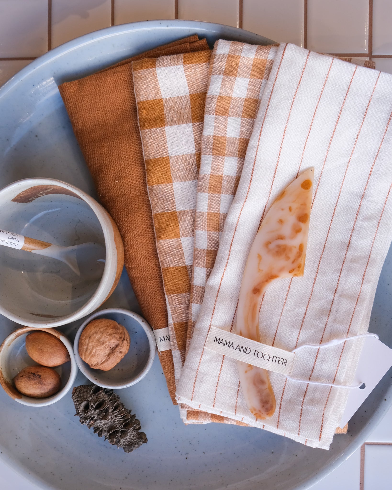 Set of patterned  linen tea towels on a blue platter with small Palinopsia Ceramics bowls and items.