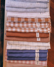 Stack of folded linen tea towels in various patterns and colours on a wooden surface.