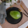 Still life photo of a green papaya on a black dinner plate by Palinopsia ceramics  