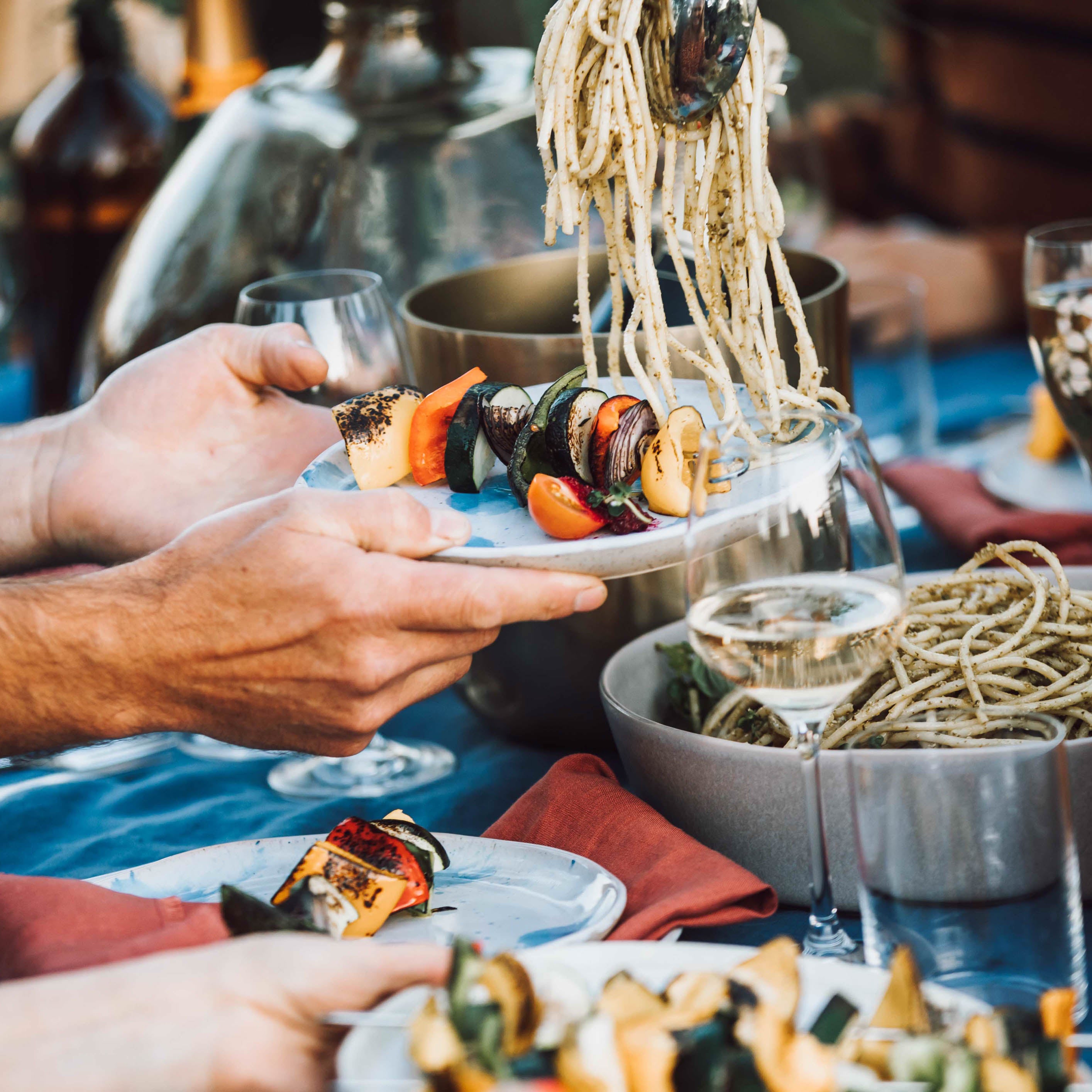 Busy dinner table with pasta salad and grilled vegetables on handmade Palinopsia Ceramic plates 