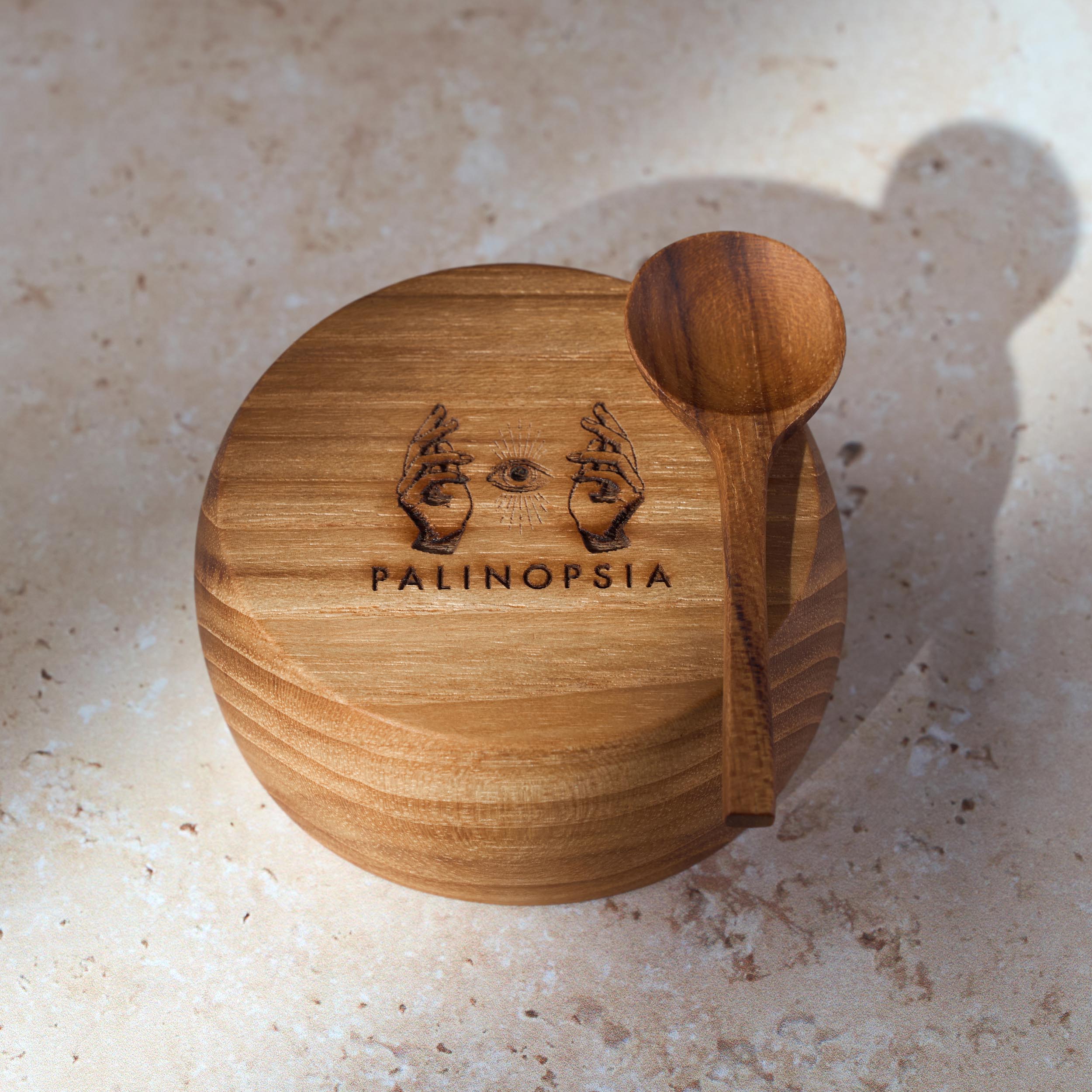 Detailed shot of a small teak wooden bowl and spoon with the Palinopsia logo on the bottom.