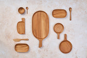 A mix of Palinopsia wooden teak serving trays, knives, and cheese boards on a light stone background.