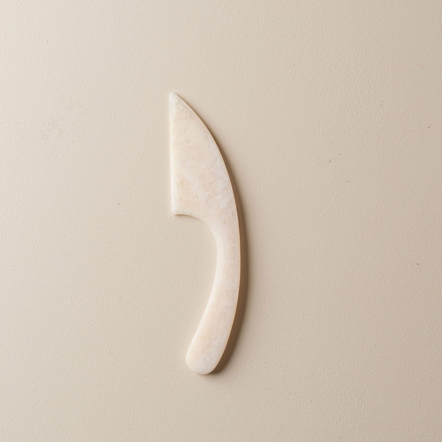 White and light pink resin cheese knife on a beige background
