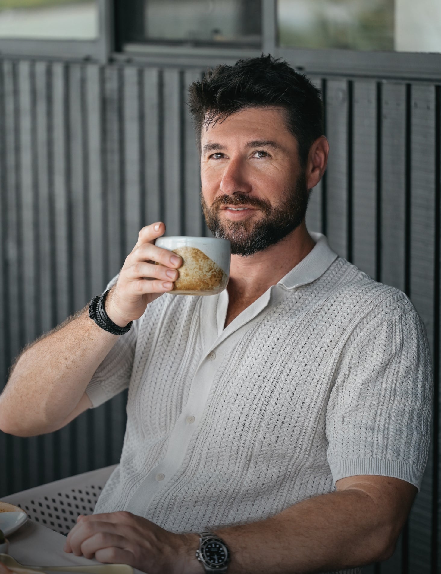 Man drinking from a Palinopsia ceramic cup outdoors with a blurred weatherboard house background