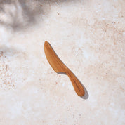 Bird’s-eye view of a Palinopsia wooden teak cheese or butter knife on a light stone background.