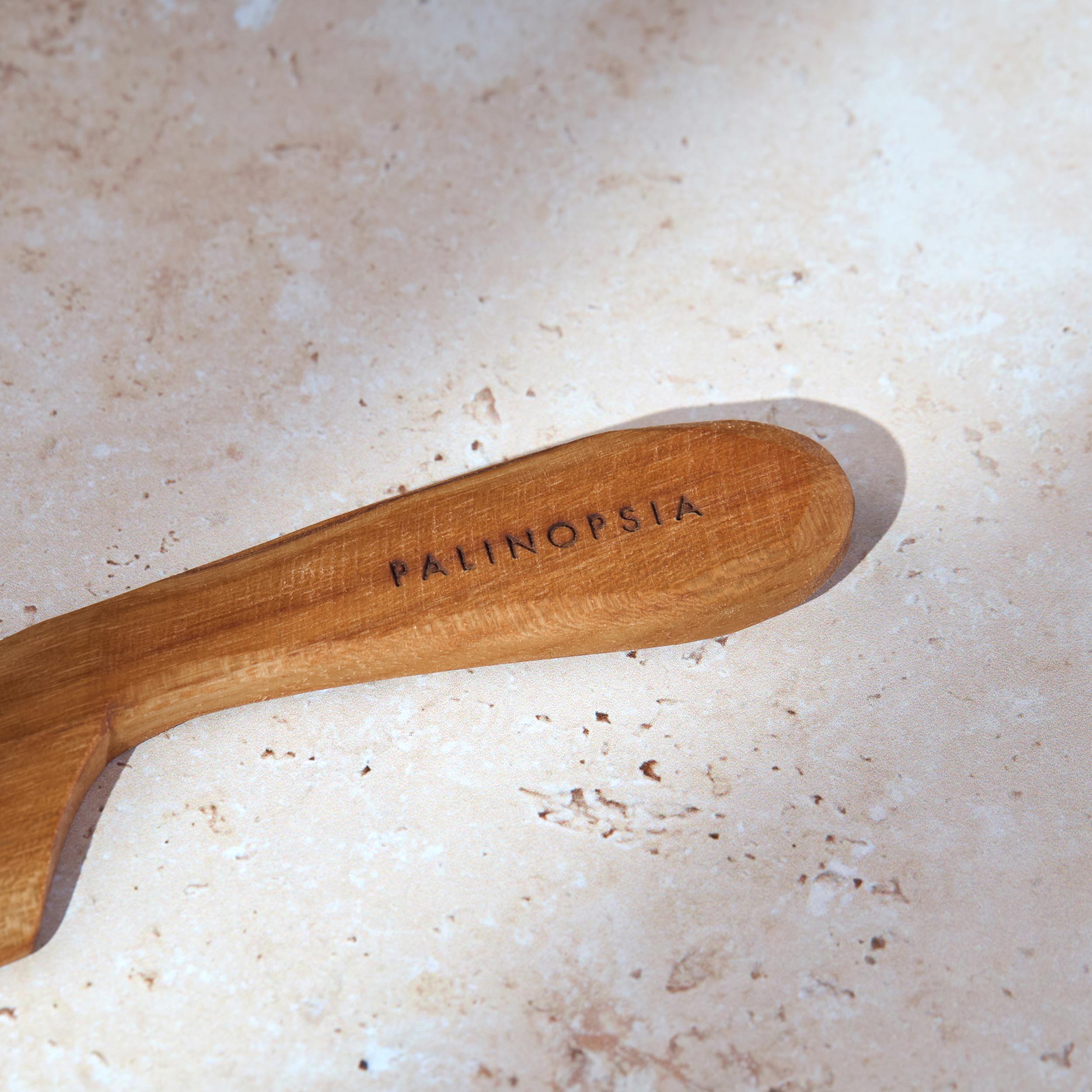 Close-up shot of the handle of a teak wooden cheese or butter knife with a Palinopsia label on the handle.