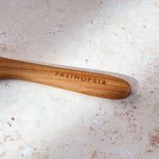 Close-up shot of the handle of a teak wooden spreading knife with a Palinopsia label on the handle.