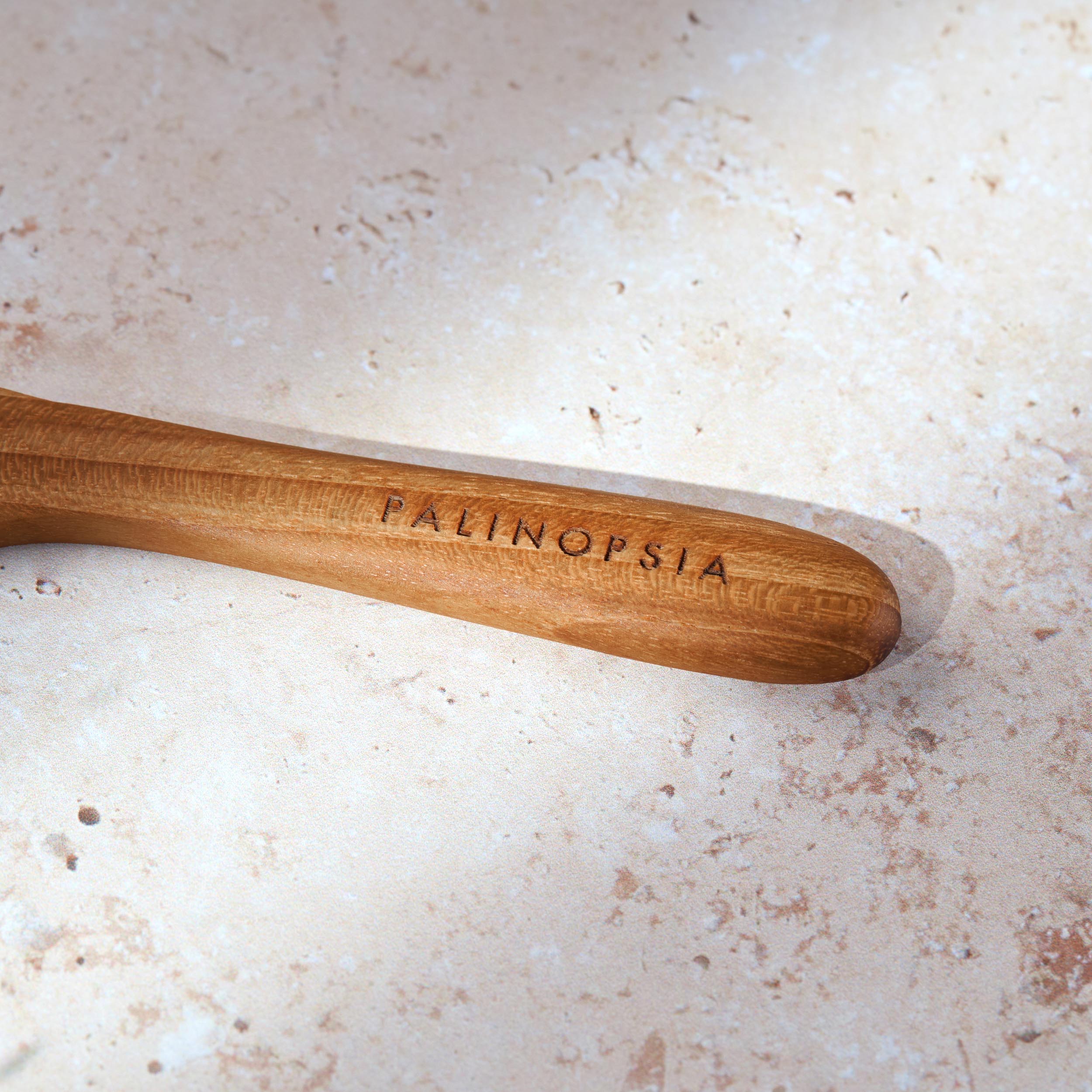 Close-up shot of the handle of a teak wooden spreading knife with a Palinopsia label on the handle.