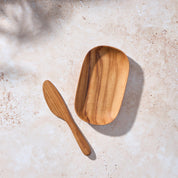 Bird’s-eye view of a Palinopsia teak wooden serving tray and knife on a light stone background.