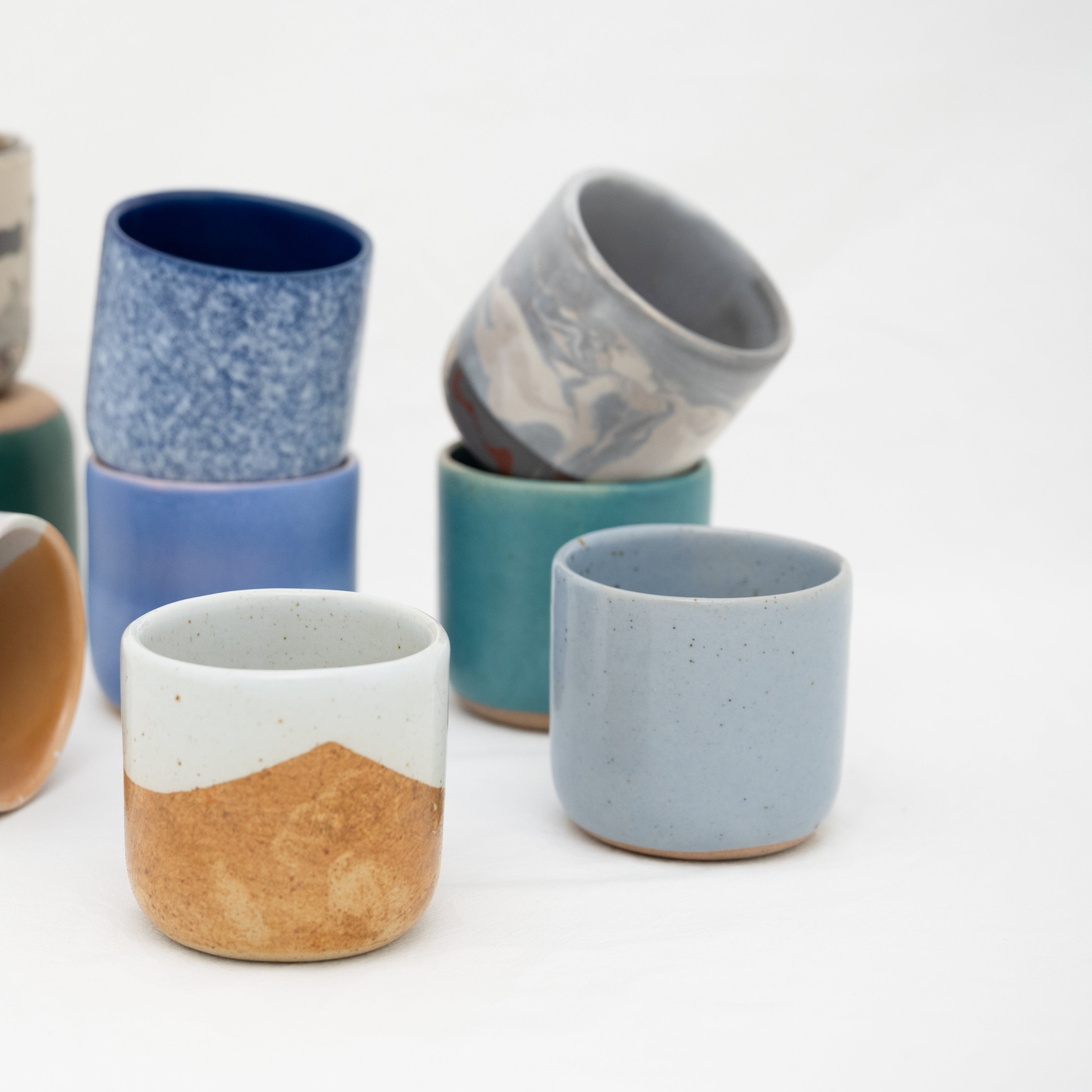 Set of ceramic espresso cups with various colours and patterns on a white background