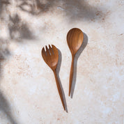 Bird’s-eye view of a set of large teak wooden salad servers on a light stone background.