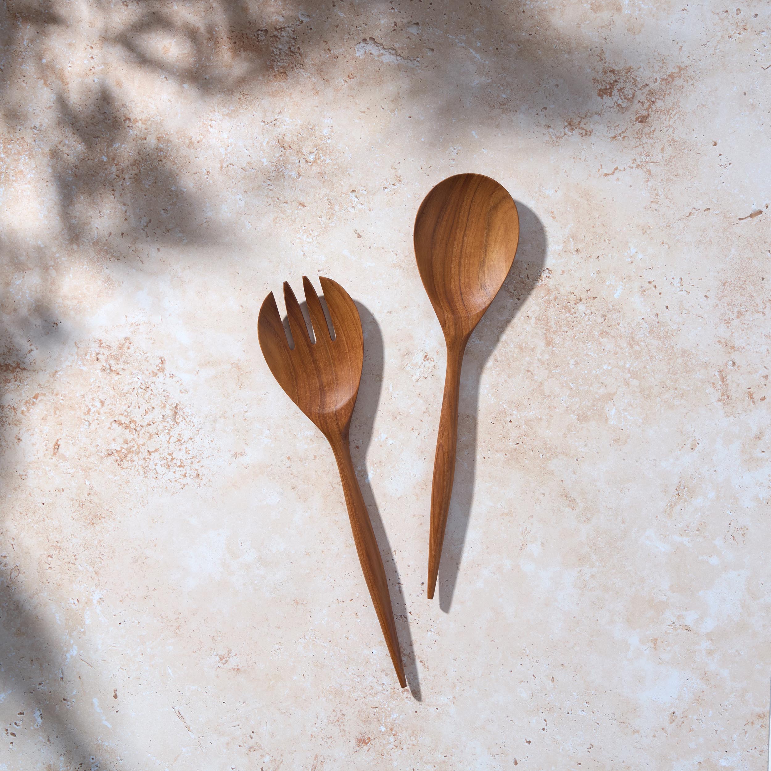 Bird’s-eye view of a set of large teak wooden salad servers on a light stone background.