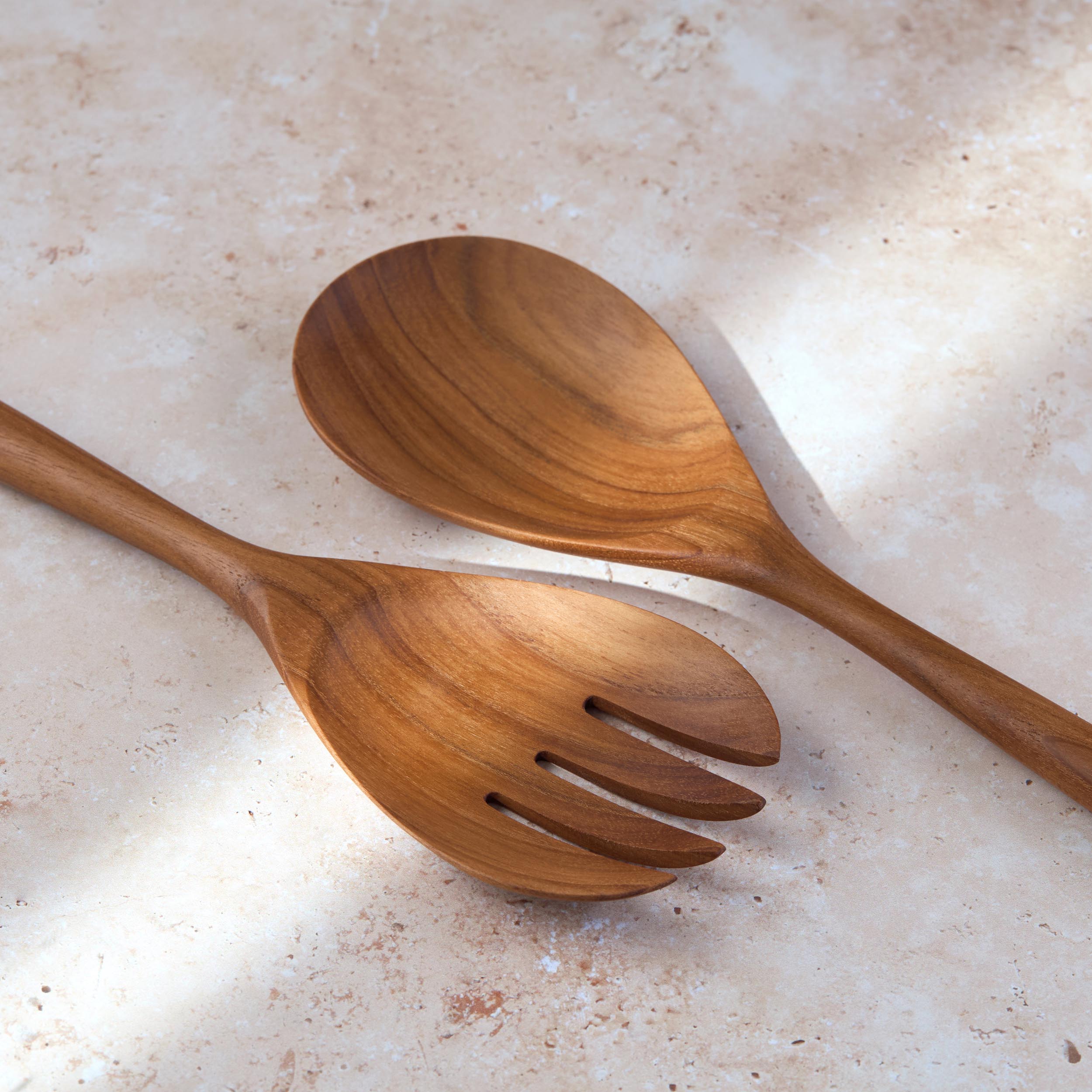 Detailed shot of a large teak wooden salad serving set by Palinopsia on a light stone background.