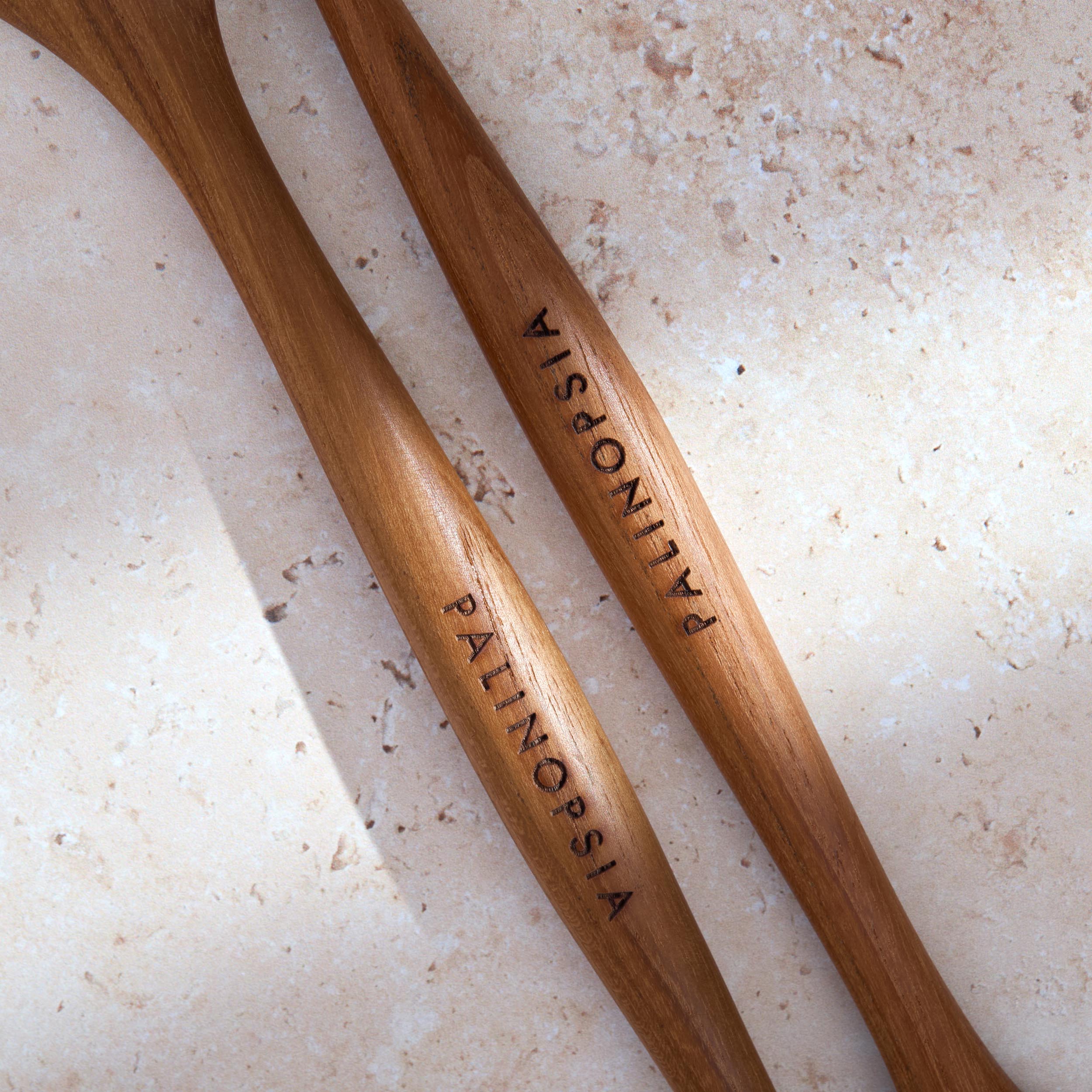 Close-up shot of the handles of large teak wooden salad servers with Palinopsia labels on the handles.
