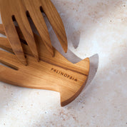 Close-up shot of a teak wooden salad serving set with the Palinopsia label on a light stone background.