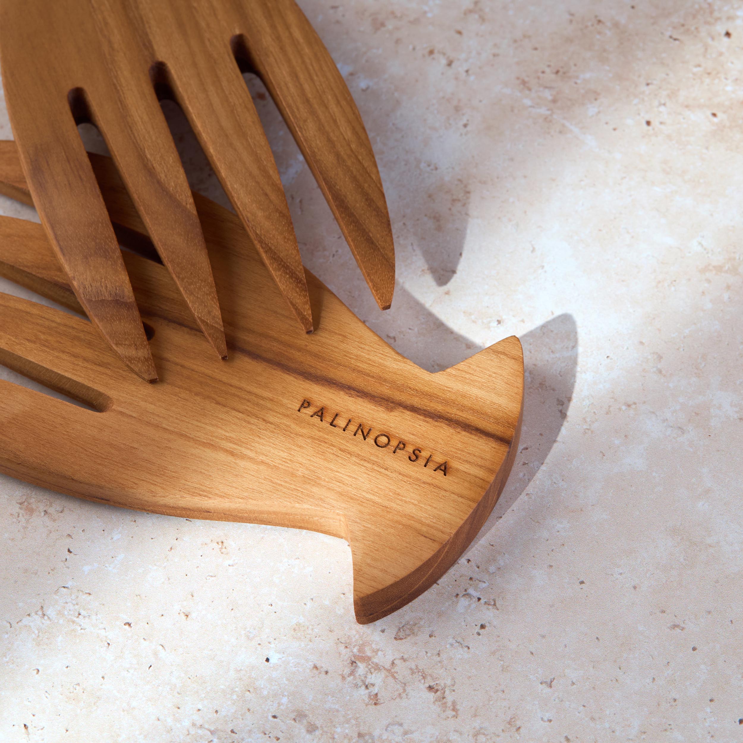 Close-up shot of a teak wooden salad serving set with the Palinopsia label on a light stone background.