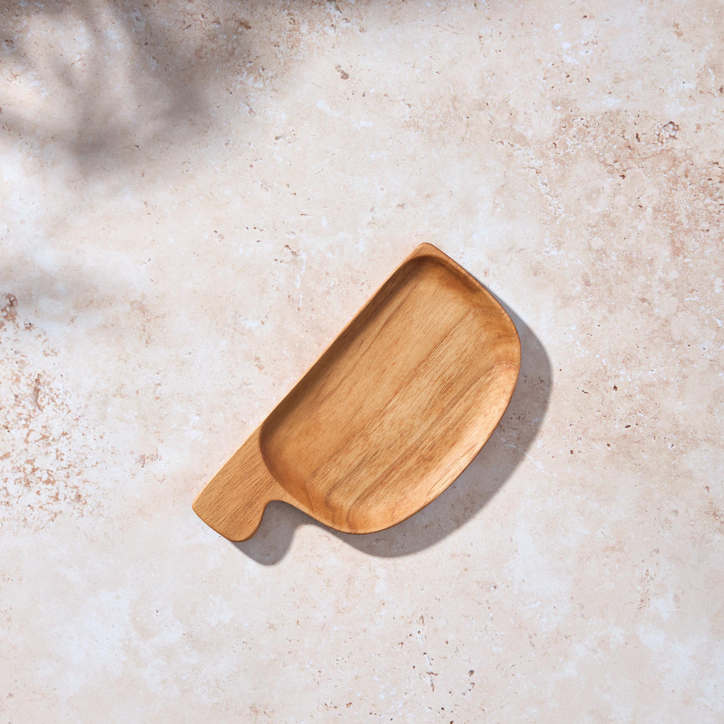 Bird’s-eye view of a Palinopsia teak wooden small rectangular serving tray with a handle on a light stone background.
