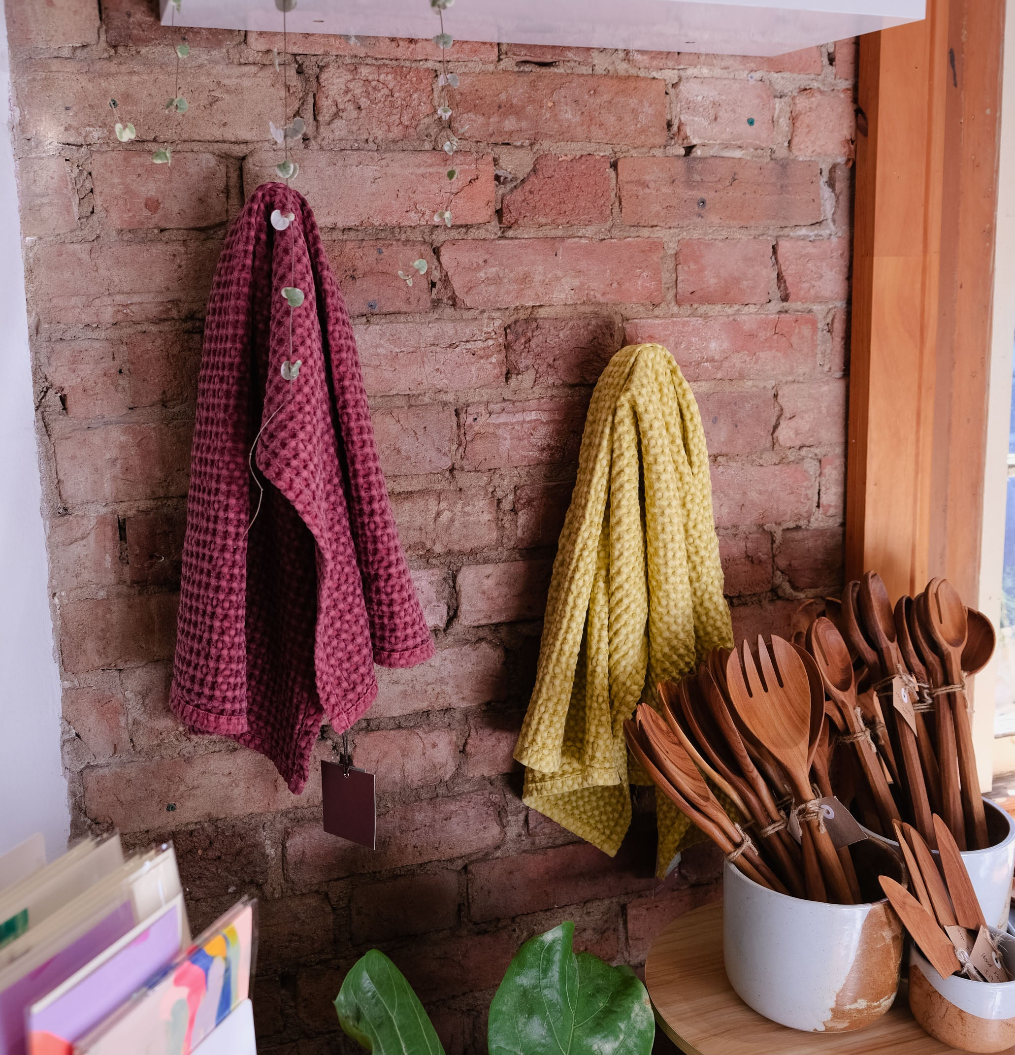 Two textured kitchen towels, one wine burgundy and one mustard yellow, hanging on a rustic red brick wall in Palinopsia Ceramics store that looks like a styled kitchen setting.