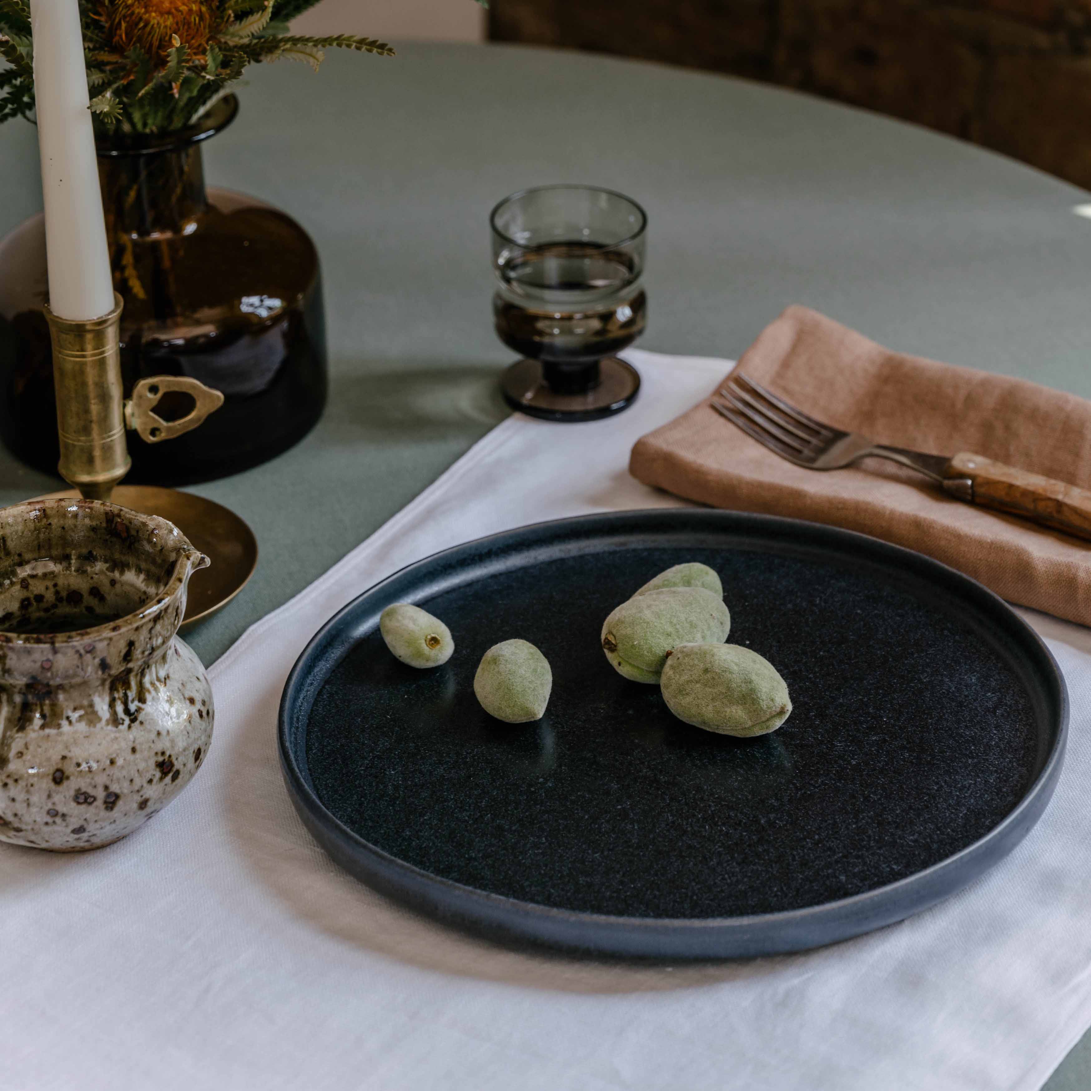Table setting by  Palinopsia Ceramics displaying their Australian made linen collection of table cloths, placemats and napkins with a black handmade plate and still life setting in Sydney Australia 