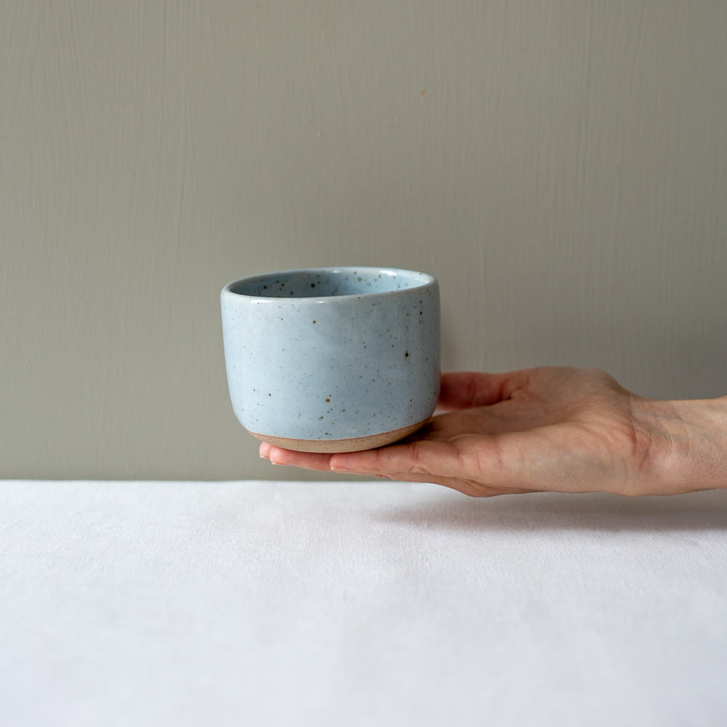 A hand holding out a coffee cup with no handle by Palinopsia Ceramics 