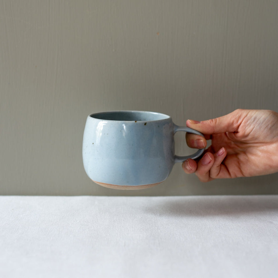 Hand holding a handmade Palinopsia coffee mug in blue speckle 